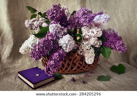 Still life: a lush bouquet of lilacs in a wicker basket and book on a linen background