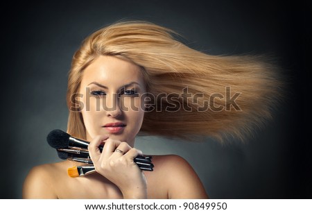 woman with long blowing hair  and with make-up brushes near attractive face