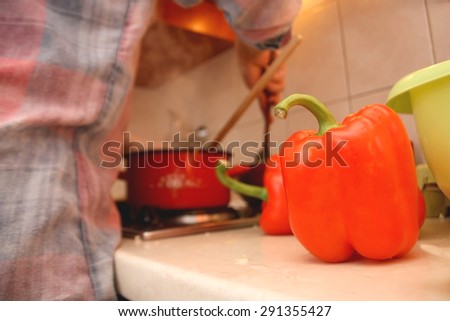 Two red peppers in the kitchen, cooking process in the background. Selective focus.