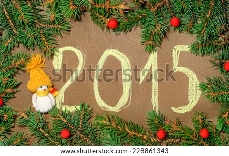 Christmas 2015 inscription on the wooden background in a frame of fir branches, red beads and a snowman in a yellow cap