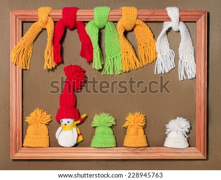 Christmas card with hats, scarves and a snowman in the frame in on the wooden background