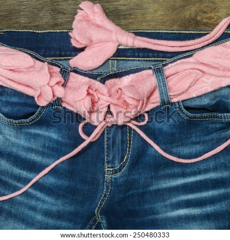 pink felted  belt with roses in blue jeans on the wooden background