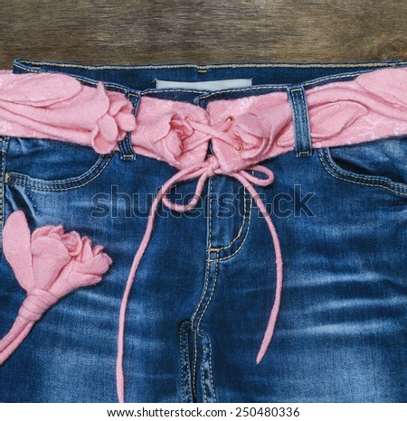 pink felted  belt with roses in blue jeans on the wooden background