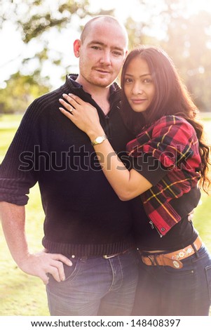 Happy young couple portrait, asian woman, caucasian man, hugging tenderly in outdoor environment and beautiful light
