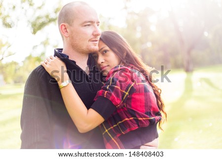 Romantic young couple portrait, asian woman, caucasian man, hugging tenderly in outdoor environment and beautiful light