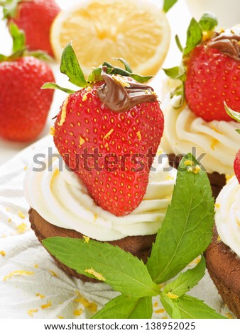 Chocolate cupcakes with strawberries, cocoa-nut paste and whipped cream. Shallow dof.