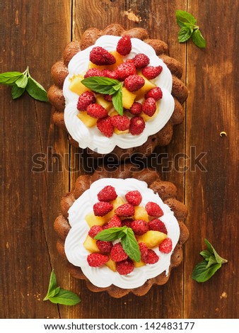 Coconut cakes with whipped cream, peach and wild strawberries. Viewed from above.