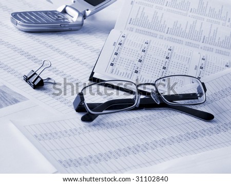 Glasses, daily book and mobile phone on financial documents. Toned blue. Shallow DOF.