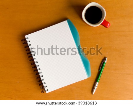 Coffee cup, spiral notebook and pen on the wooden table. Viewed from above.
