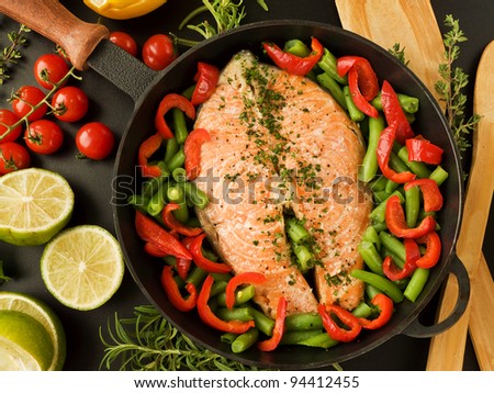 Frying pan with salmon steak, stir-fry veggies and herbs. Viewed from above.