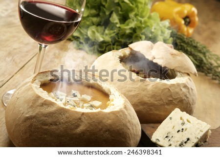 SOUP IN BREAD - Hot vegetable soup served in bread with a glass of red wine and vegetables and salad in the background
