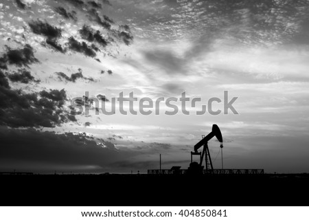 Cloudy sunset and silhouette of crude oil pump unit in oilfield - Black and white