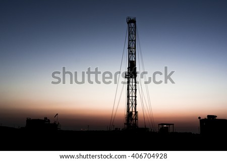 Sunset and silhouette of drilling rig in oilfield