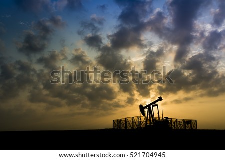 Silhouette of crude oil pump in oilfield at cloudy sunset.