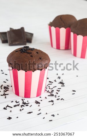 Chocolate muffins in pink striped muffin paper on a table with chocolate pieces.