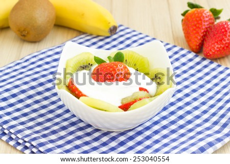 Fruit salad with kiwi, banana, strawberry and yogurt sauce on a blue checkered table cloth.