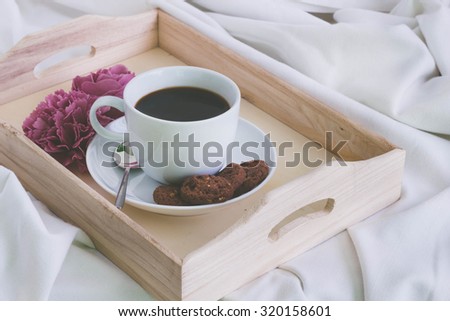 Wooden tray with a cup of coffee and cookies on a bed