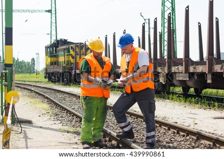 Rail workers coordinating cargo loading to transport train on the tracks. Railway employees in safety west and helmet talking about instructions.