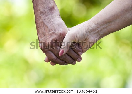 clasped hands of older people with natural background