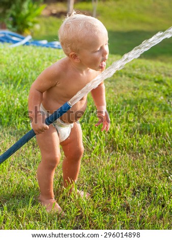 Little cute child boy playing with a rubber hose in the garden