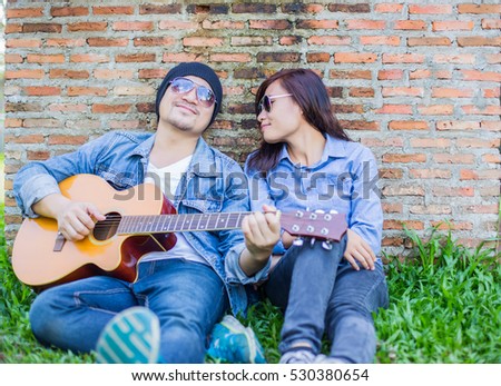 Hipster man teach playing the guitar to his girlfriend while sitting in the grass look so happy. Couple in love concept.