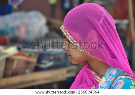 Jodhpur, Rajasthan, India - October 17, 2013: Young married Indian woman with bright pink head scarf doing her daily purchases at a street market in Jodhpur's city centre