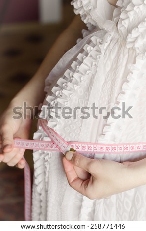 Pregnant woman in white shirt measures the belly of tape