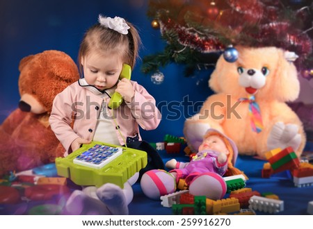 surprised little girl in purple jacket holding a green phone with toys on a blue background