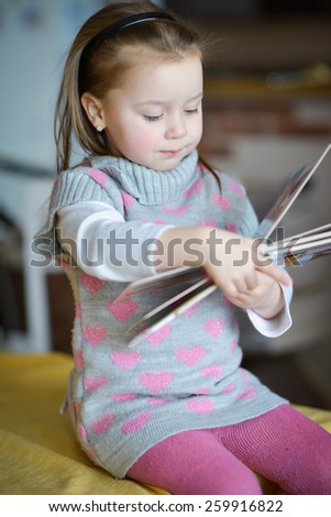 little girl with positive emotions sitting at the table reading a book
