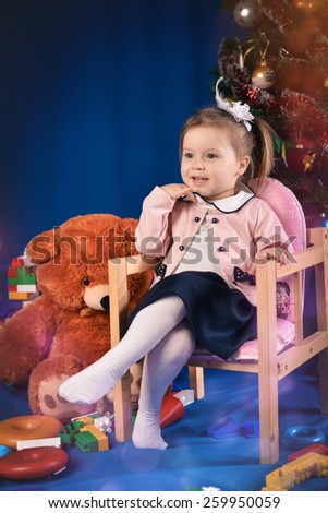 surprised little girl in purple jacket sitting on chair with toys on a blue background