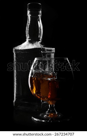 glass with ice and a bottle of cognac on black background
