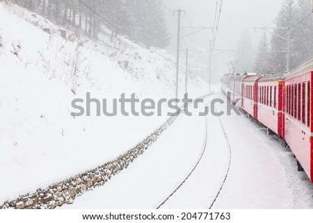 The famous Bernina red train, Unesco monument, in the middle of a winter storm