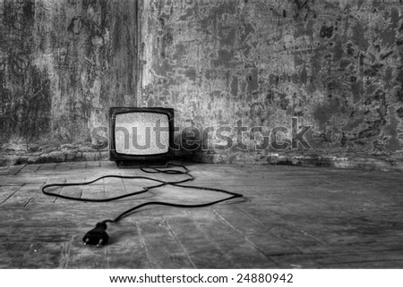 An old TV with the noise on its display standing on the dirty floor