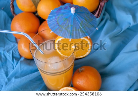 ripe orange fruits in the basket and a glass of freshly squeezed juice with a slice and umbrella