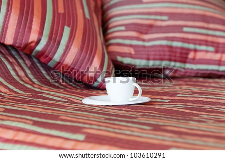 bed with two pillows, a cup of tea on the blanket