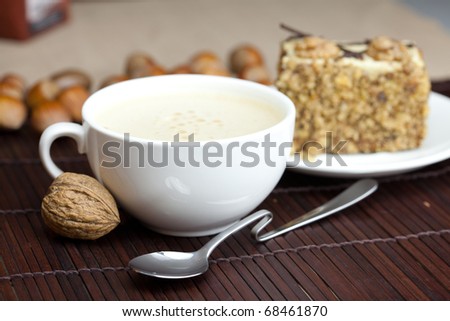 cup of cappuccino, a piece of cake with nuts on a plate lying on a bamboo mat