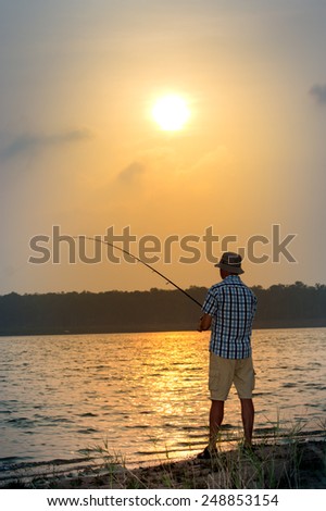 Young man fishing from a shore at sunset on the lake