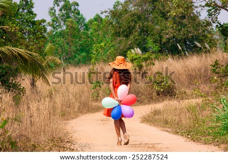 Slim beautiful young woman in hat with balloons is going along a dusty road, soft focus