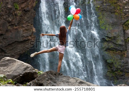 The young woman with balloons on the background of the waterfall