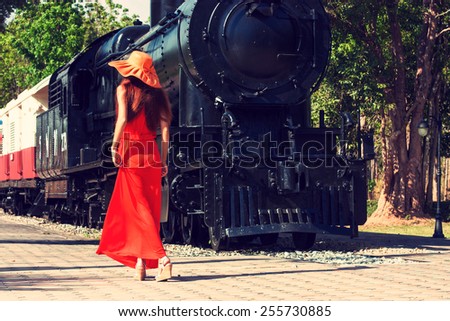 Young woman in red dress and hat waiting train on the platform of railway station. Retro style