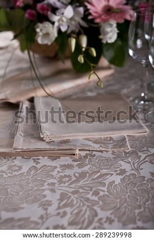 Luxury beige serviettes on the beige pattern table-cloth with flowers