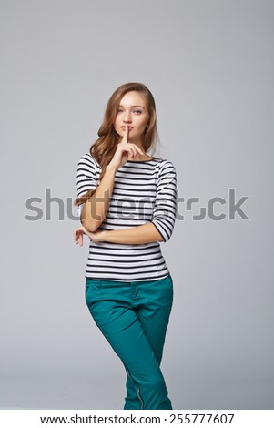 Young woman with finger on lips, on gray background