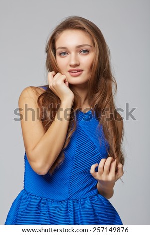 Young stylish slim tanned female standing with hand on chin, on gray background