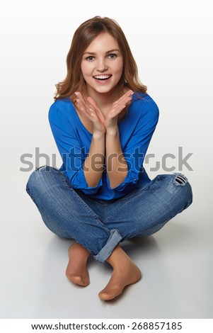 The front view of the smiling beauty who sits on a floor on a gray background with a hand on a chin