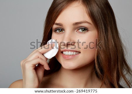 Pretty young woman removing make up, on gray background