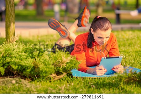 fitness, technology, people and sports concept - the smiling woman with the tablet PC computer, lying on a mat in the open air