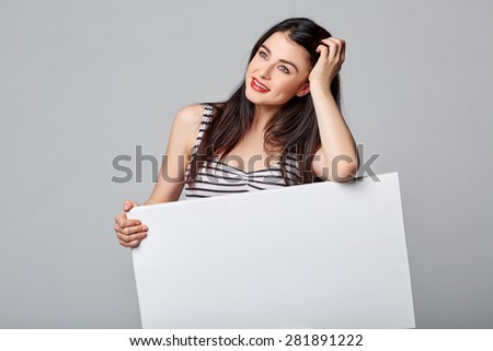 Full length of beautiful woman standing behind, holding white blank advertising board banner, on gray background