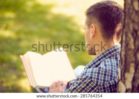 Education, people and learning concept - teenage boy or young man reading book outdoors