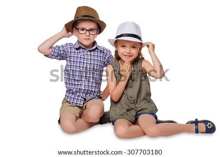 Happy boy and girl sitting together on the floor in their hats, isolated on white background.