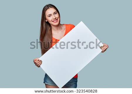 Young woman holding white blank cardboard, over gray background.